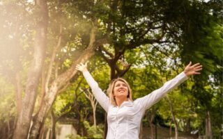 Mulher sorridente com braços abertos em parque urbano com árvores