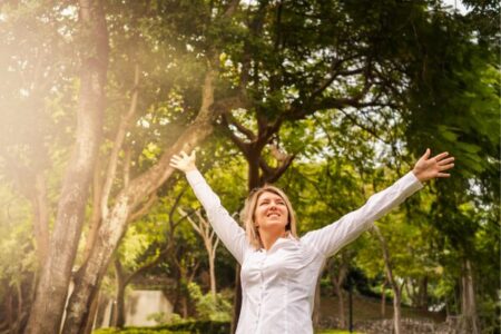 Mulher sorridente com braços abertos em parque urbano com árvores