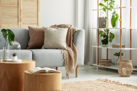 Sala compacta decorada com sofá cinza, prateleira vertical com plantas e móveis de madeira clara