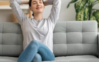Mulher relaxando em sofá claro, em sala com decoração simples e planta ao fundo, representando o estilo de vida do minimalismo consciente
