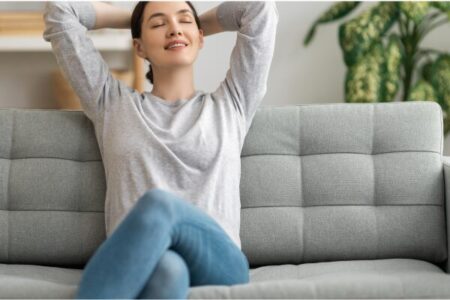 Mulher relaxando em sofá claro, em sala com decoração simples e planta ao fundo, representando o estilo de vida do minimalismo consciente