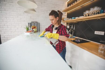 Mulher realizando limpeza rápida em cozinha com luvas amarelas e spray